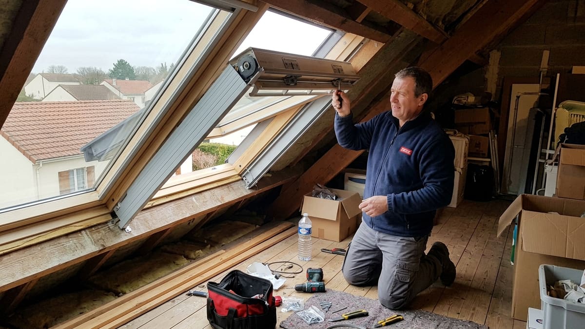 Technicien réparant le volet roulant solaire d'un Velux à l'intérieur d'un grenier